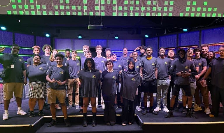 A cohort of students from the Launchpad Program standing in from of a purple and green led stage